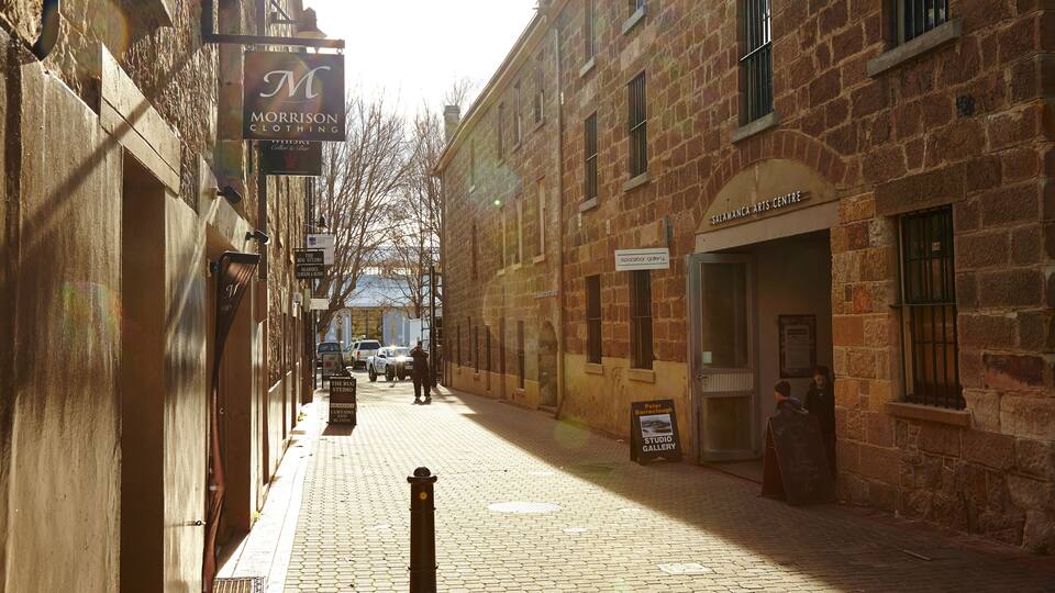 A cobblestone street lined with historic stone buildings, including a Morrison Clothing store and a gallery.
