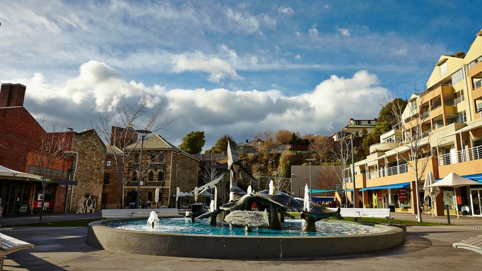 A public square with a central fountain, surrounded by buildings and trees.