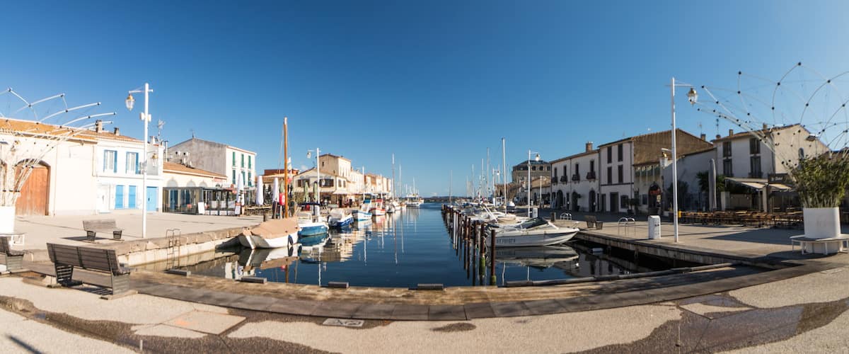 A marina with boats docked, waterfront buildings, and a clear blue sky.