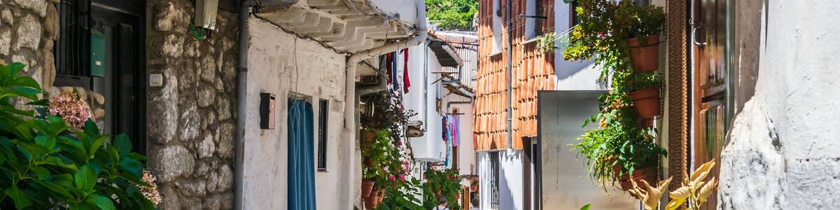 Une ruelle étroite pavée, bordée de bâtiments aux murs de pierre et aux poutres apparentes, agrémentée de plantes en pot et de linge suspendu.