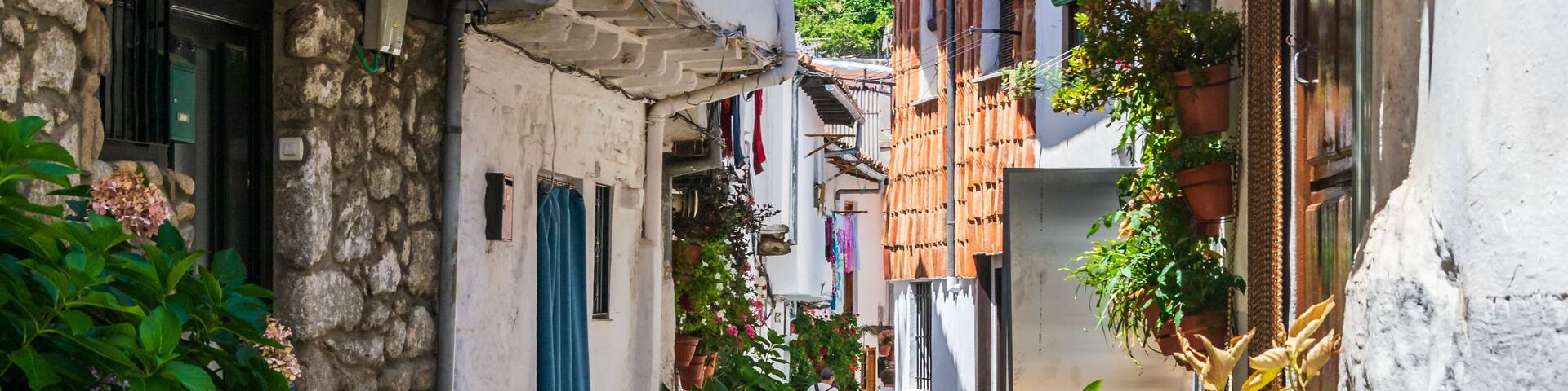 A narrow cobblestone street flanked by buildings with stone walls and wooden beams, potted plants, and hanging laundry.