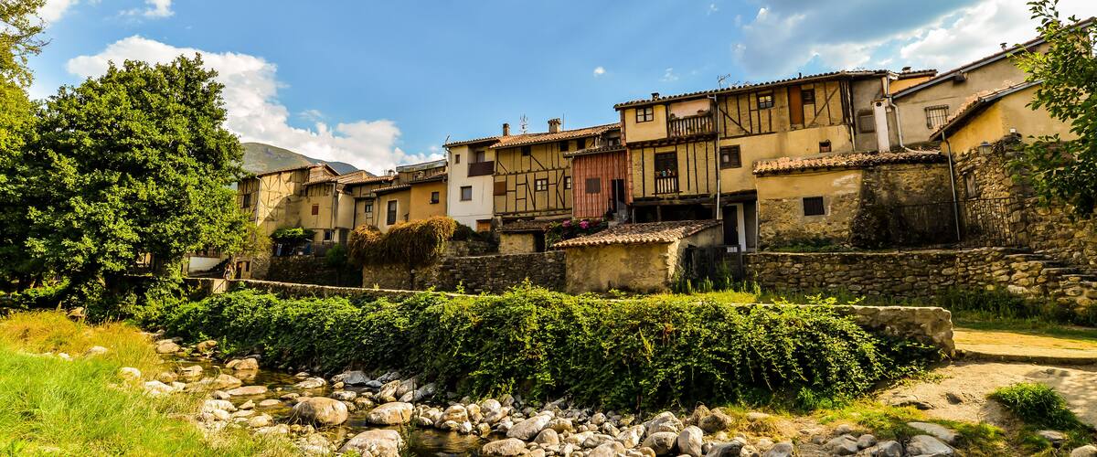 A traditional European village with stone buildings, a stream, and lush greenery.