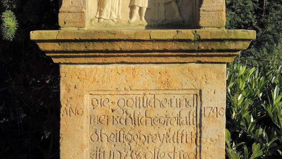 A stone monument with a relief sculpture of a man and a child, surrounded by greenery.