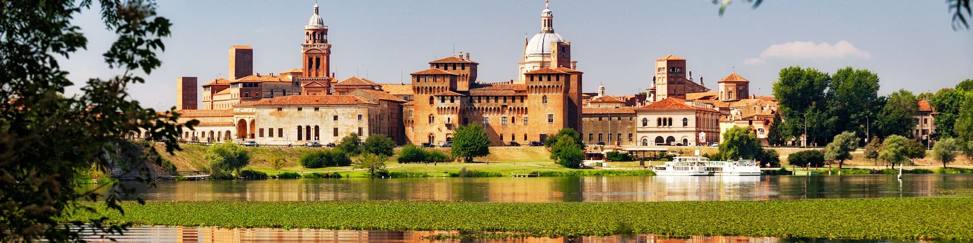 A historic building complex with a large body of water in the foreground, surrounded by greenery.