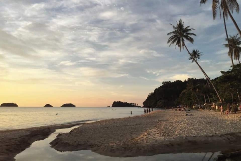 Una platja amb palmeres, aigua tranquil·la i illes allunyades.