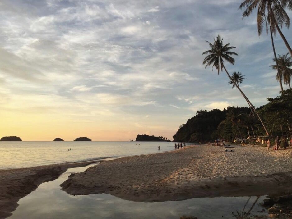 A beach with palm trees, calm water, and distant islands.