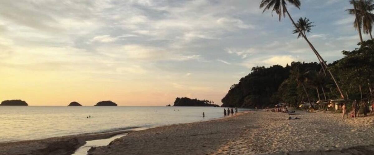 A beach with palm trees, calm water, and distant islands.