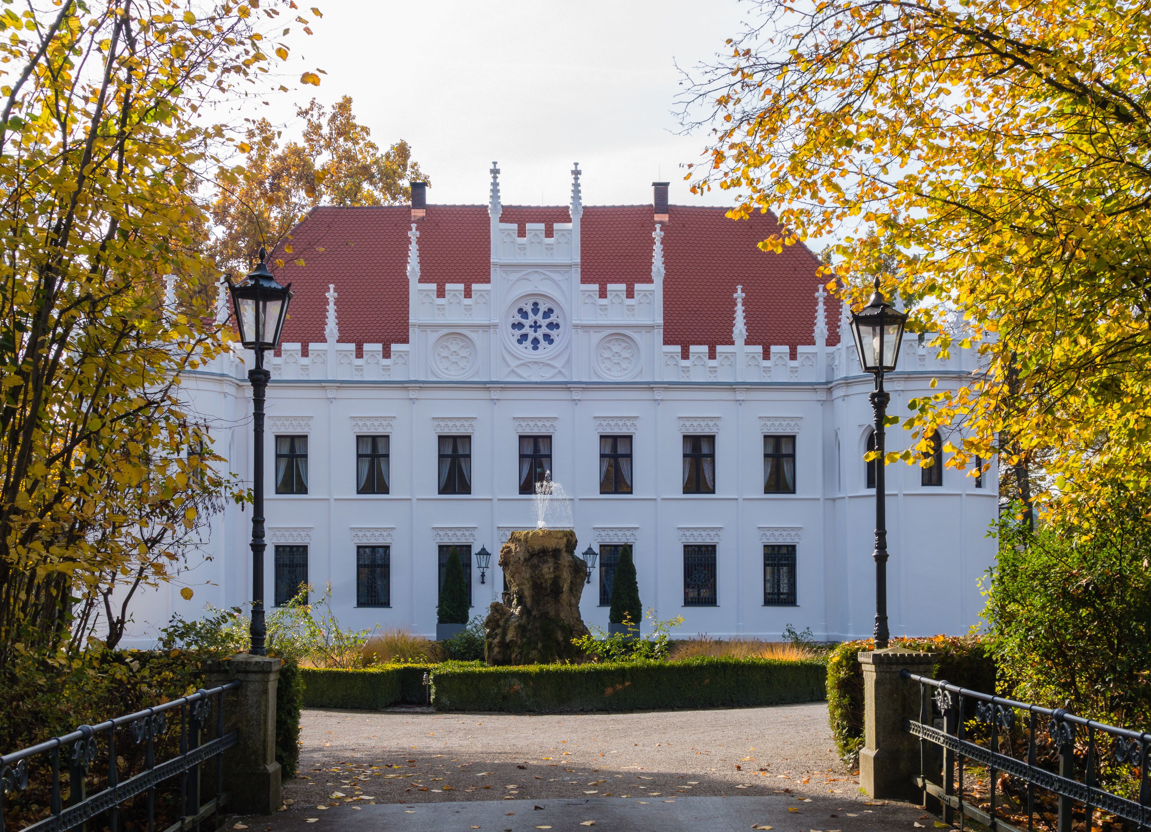A white building with a red roof, surrounded by trees with yellow leaves.