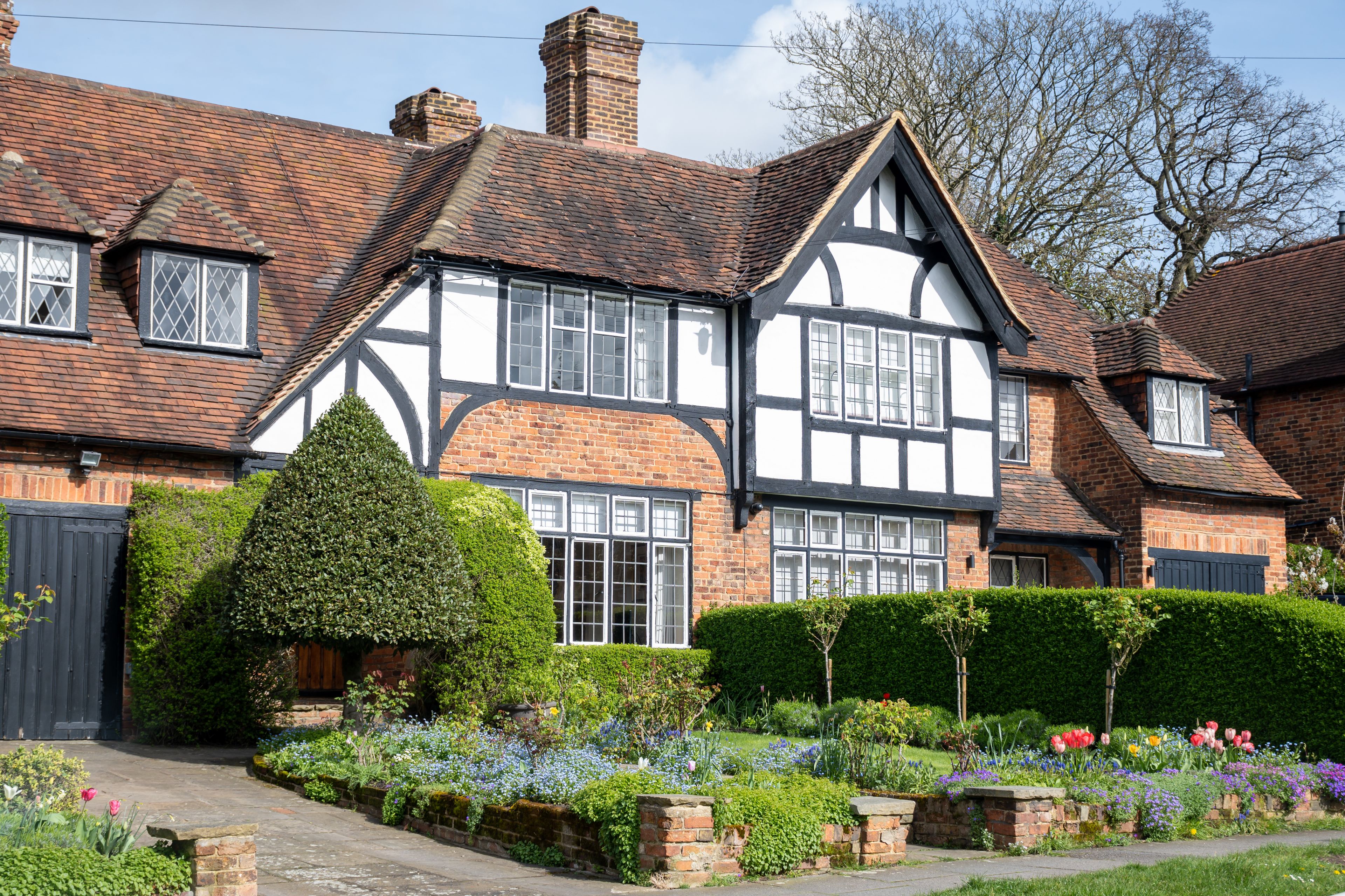Een huis in Tudorstijl met een bakstenen gevel, wit vakwerk en een verzorgde tuin met diverse bloemen en struiken.