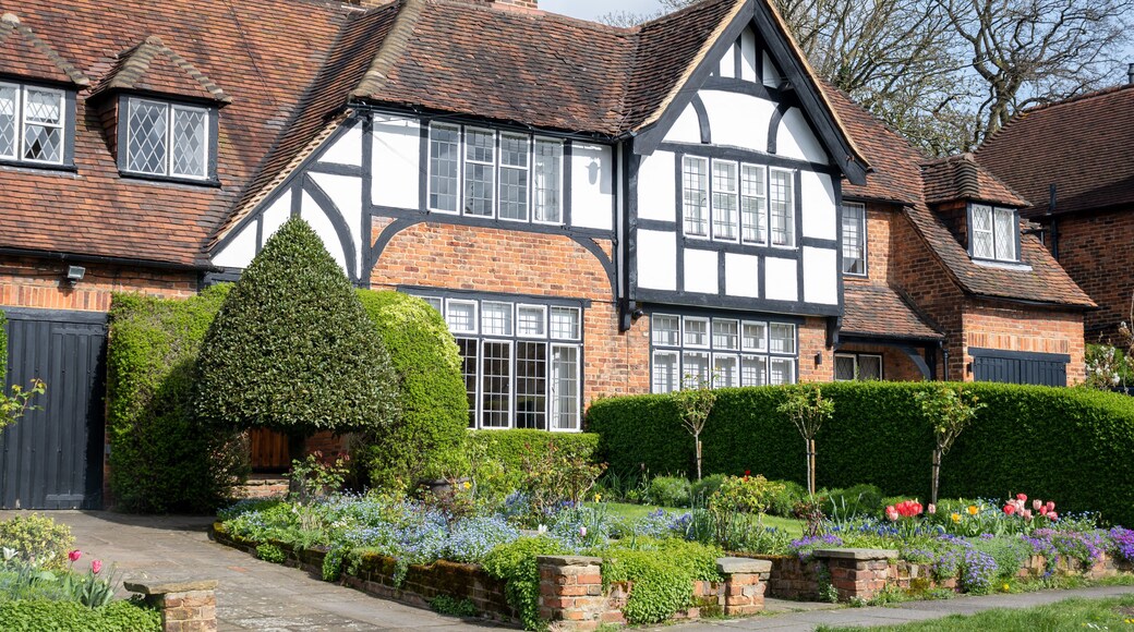 Een huis in Tudorstijl met een bakstenen gevel, wit vakwerk en een verzorgde tuin met diverse bloemen en struiken.