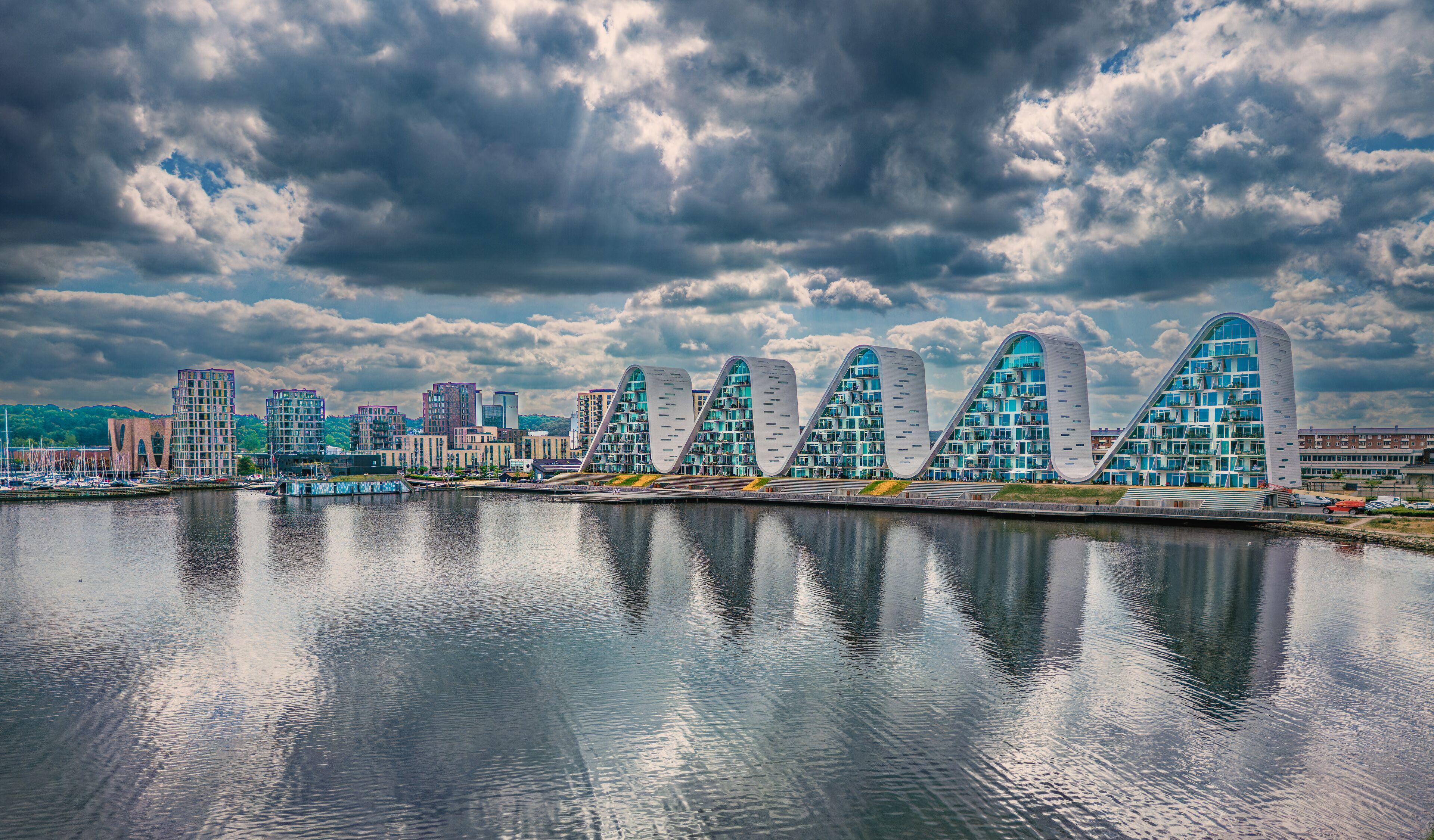 A waterfront cityscape with modern architecture, including a distinctive building with a wave-like design.