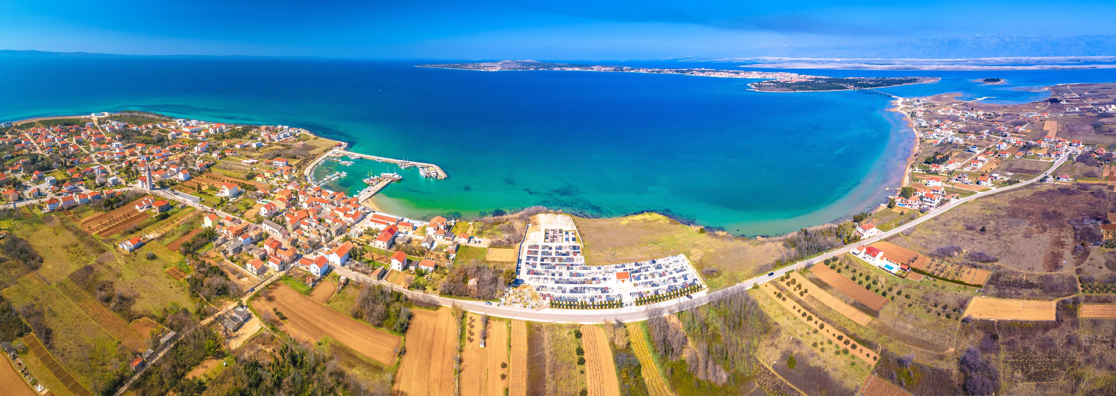 An aerial view of a coastal town with a marina, farmland, and a large body of water.