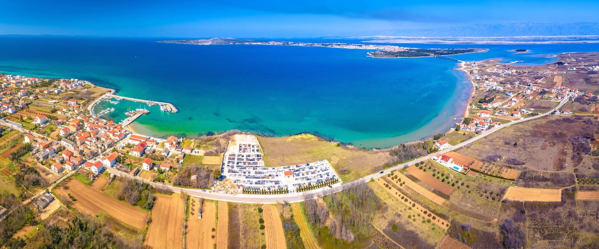 An aerial view of a coastal town with a marina, farmland, and a large body of water.