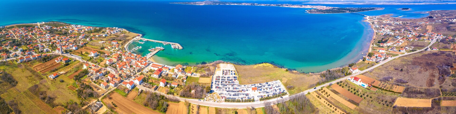 An aerial view of a coastal town with a marina, farmland, and a large body of water.