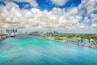 A coastal city with a cruise ship docked, clear turquoise waters, a marina, and a dense urban skyline.