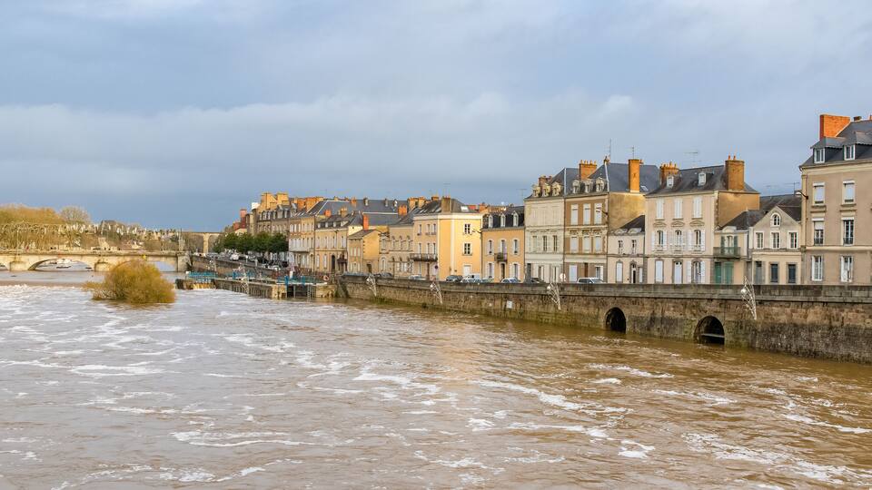 A river with a bridge, historic buildings, and a cloudy sky.