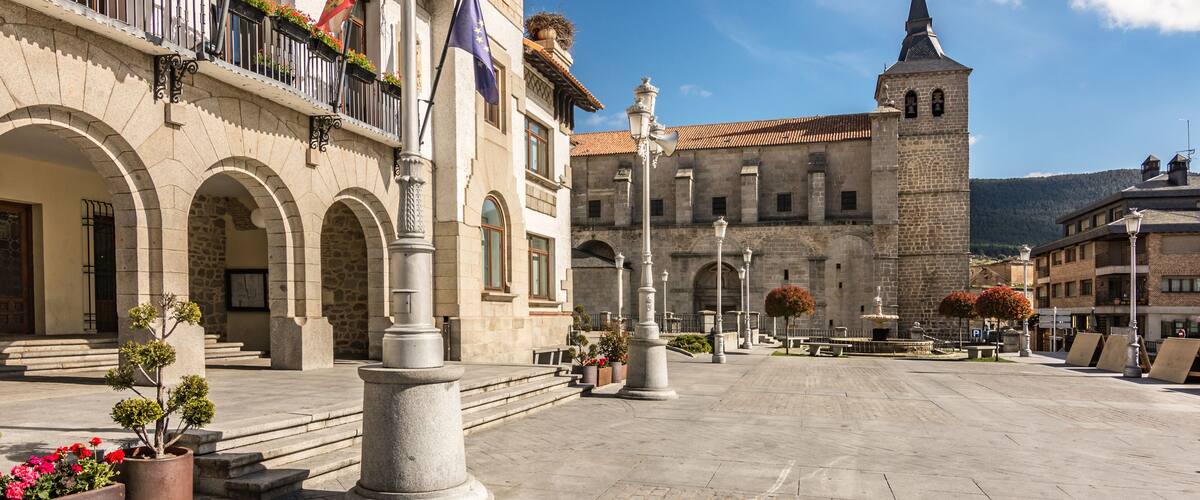 A historic square with a prominent church tower, stone buildings, and flags.