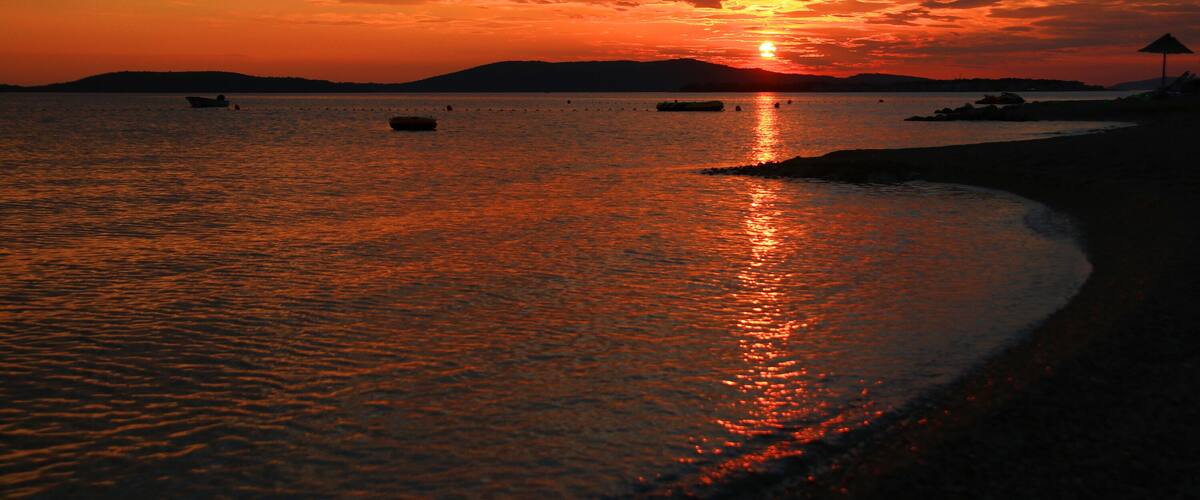 A sunset over a calm sea with boats and a beach.