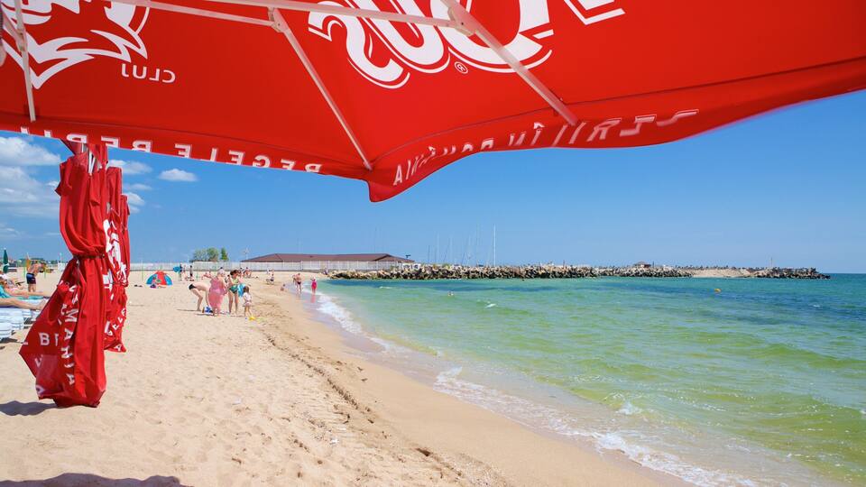 A beach with a red umbrella, clear blue sky, and calm sea.