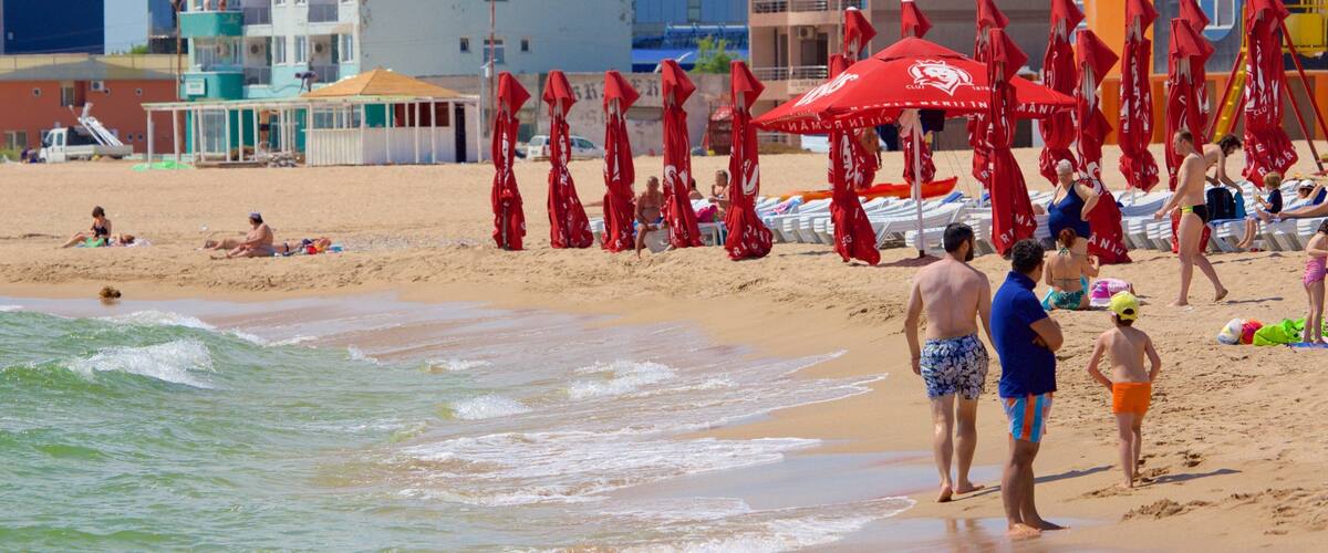 A beach with red umbrellas, people sunbathing, and buildings in the background.