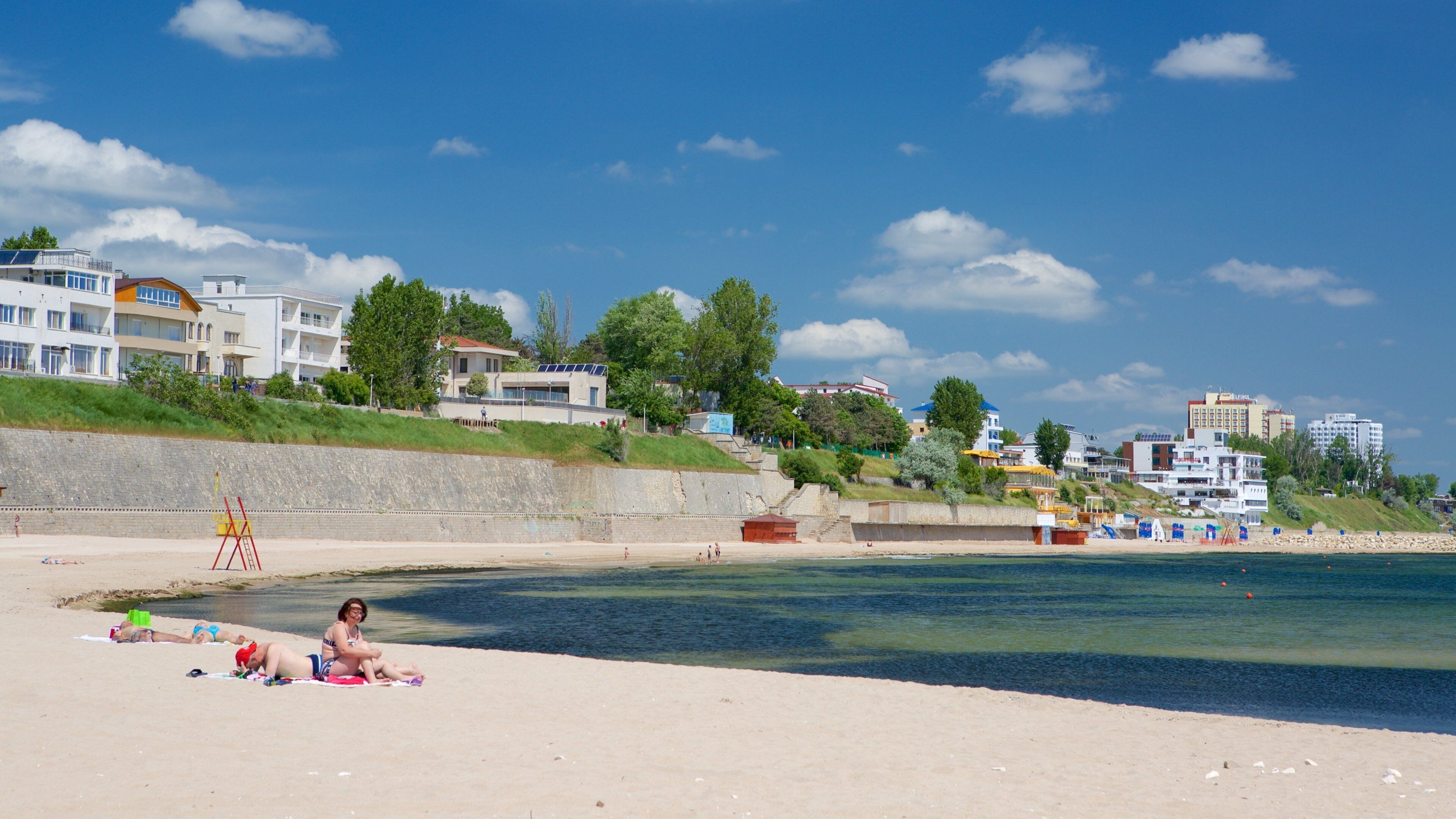 A beach with people sunbathing, a lifeguard tower, and buildings in the background.