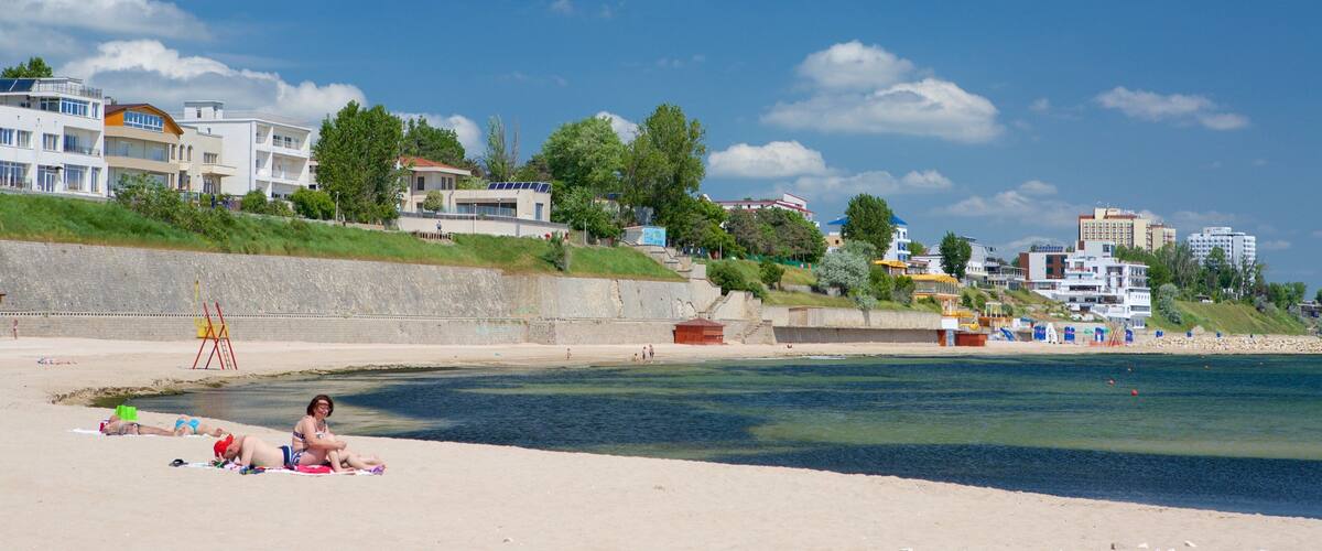 A beach with people sunbathing, a lifeguard tower, and buildings in the background.