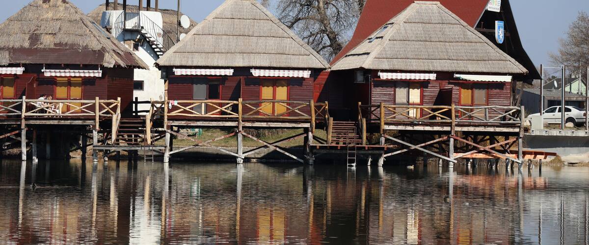 Wooden houses with thatched roofs on stilts over water, a small tower, and a clear sky.