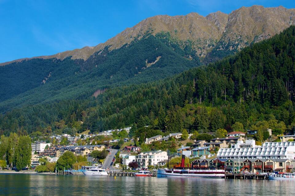 A lakeside town with boats docked, surrounded by forested mountains.