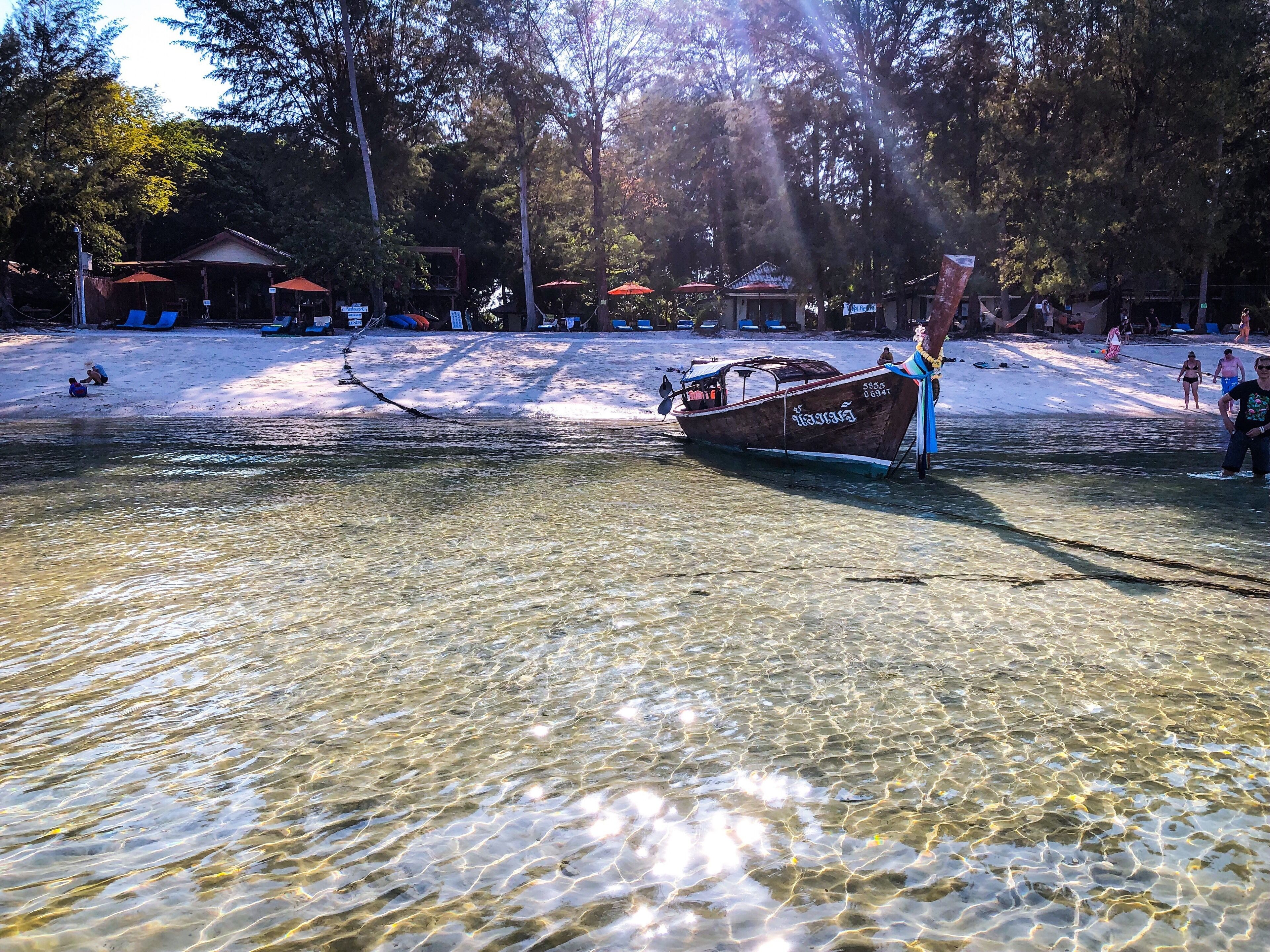 Un bote en una masa de agua clara con una playa de arena y árboles al fondo.