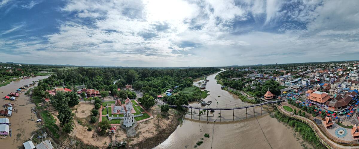 A river flowing through a town with a bridge, surrounded by greenery and buildings.