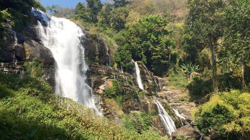 A waterfall cascading down a rocky cliff surrounded by lush greenery.