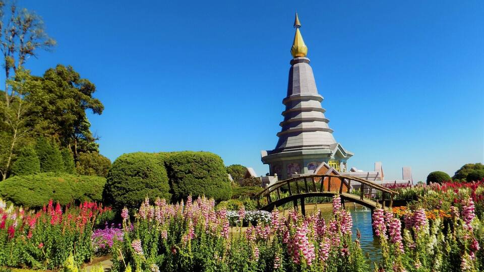 A pagoda with a golden spire, surrounded by a garden with various colorful flowers and a bridge.