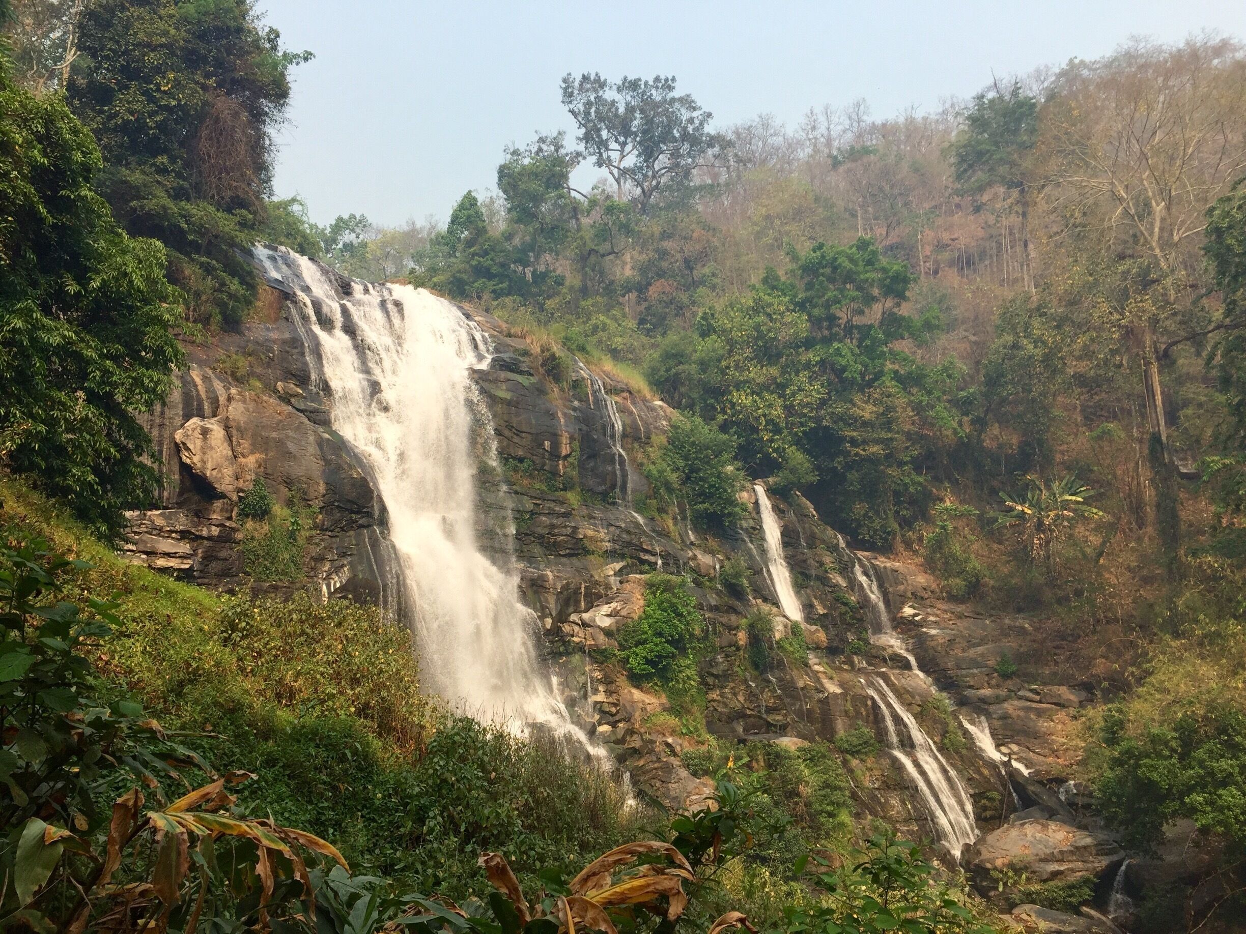 A waterfall cascading down a rocky cliff surrounded by dense greenery.