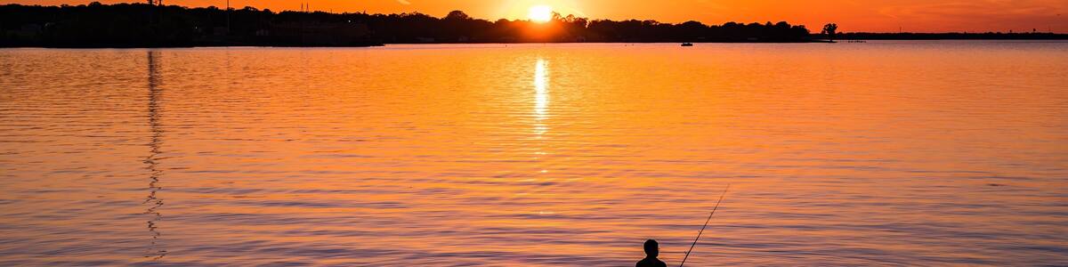 A sunset over a calm lake with a person fishing.