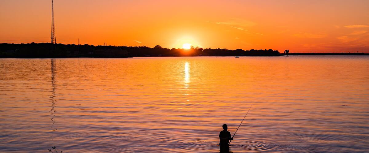 Een zonsondergang boven een rustig meer, met een visser.