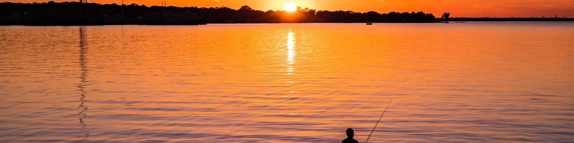 A sunset over a calm lake with a person fishing.