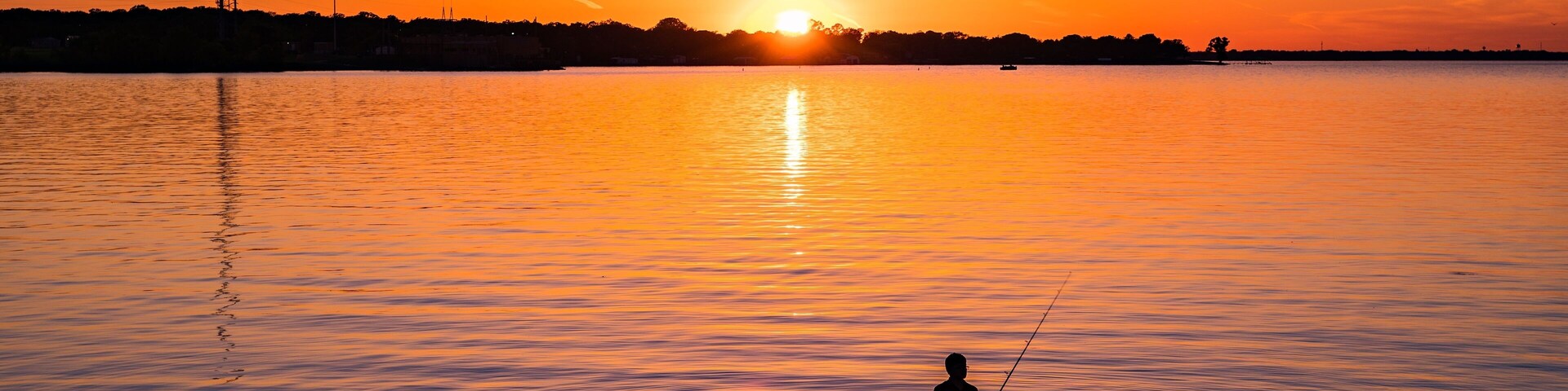 Un atardecer sobre un lago tranquilo con una persona pescando.