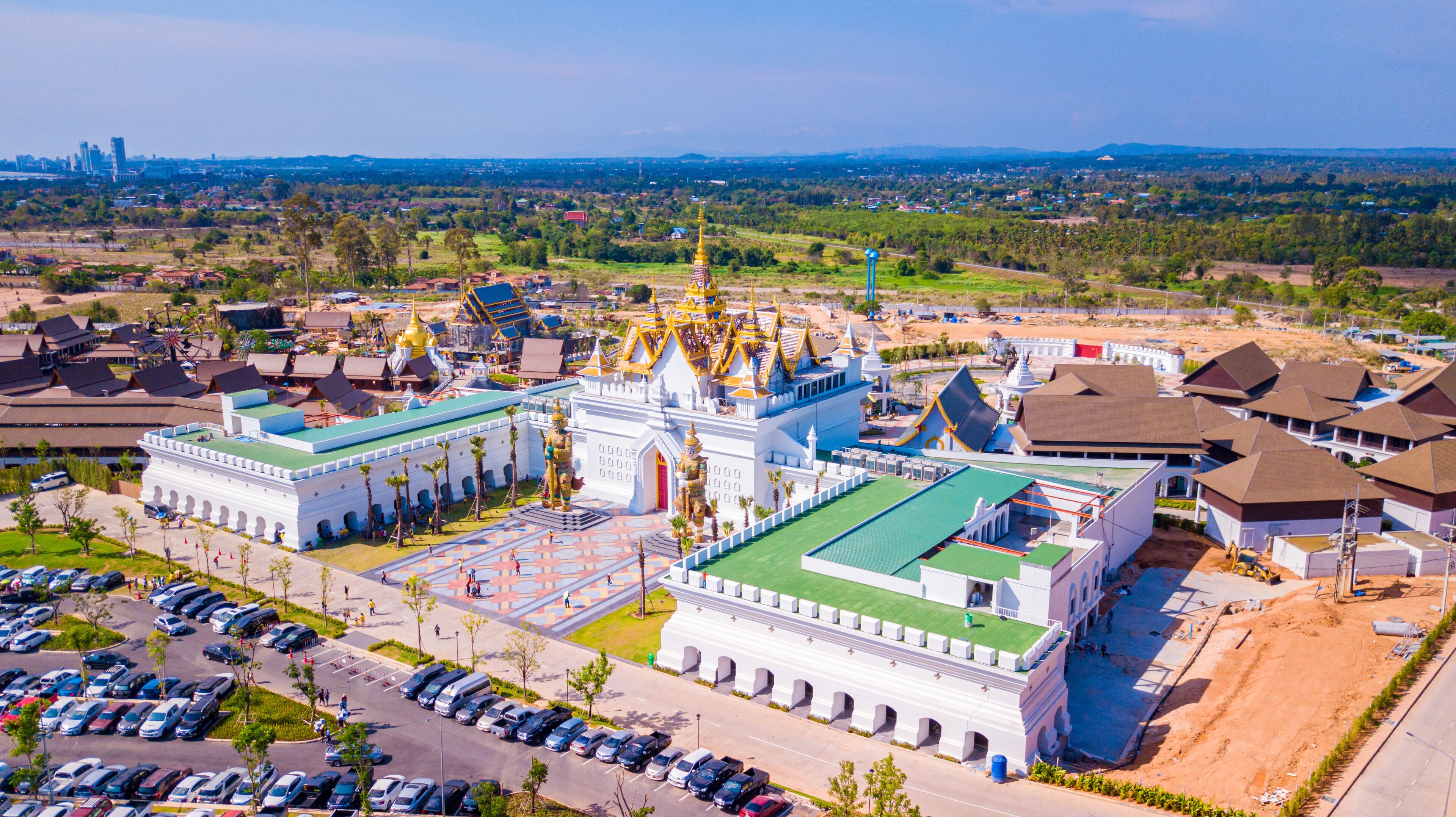 A large white temple with golden spires and a green roof, surrounded by a parking lot and residential buildings.