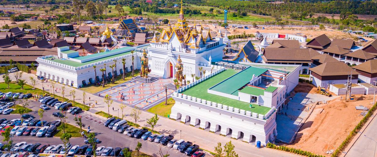 A large white temple with golden spires and a green roof, surrounded by a parking lot and residential buildings.