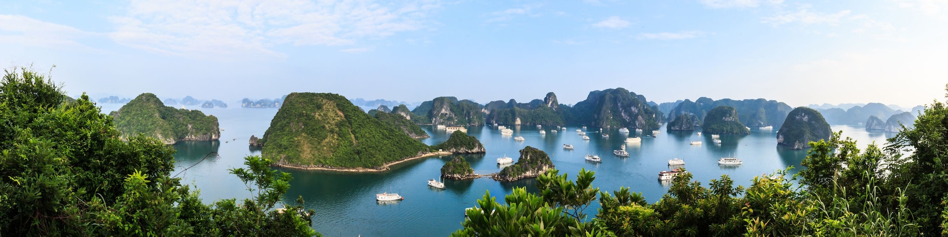 A coastal landscape with numerous boats, lush greenery, and distinctive limestone karsts.