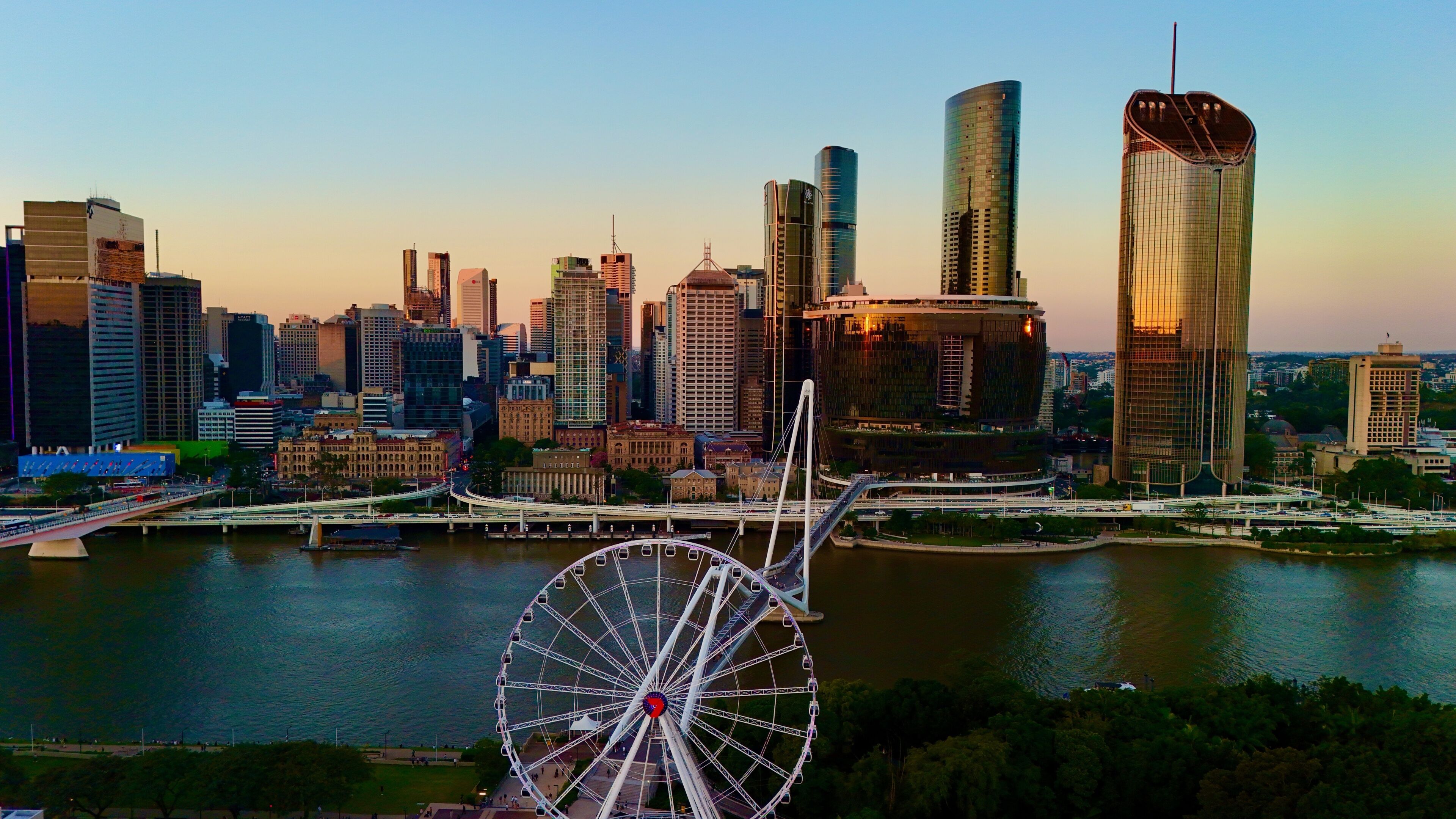 A city skyline with modern skyscrapers, a river, and a large Ferris wheel.