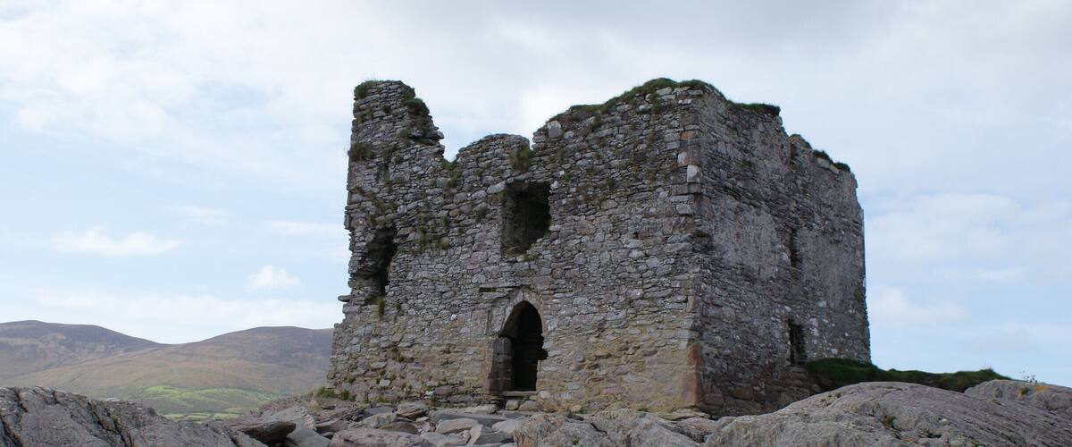 A ruined stone castle on a rocky hill with a valley in the background.