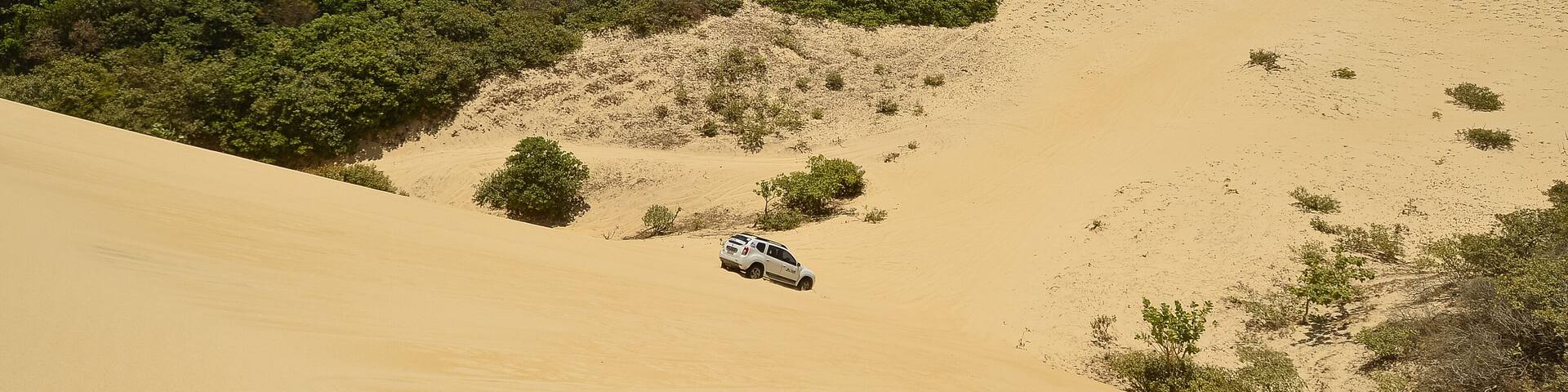 A white off-road vehicle navigating a sandy dune landscape with sparse vegetation.