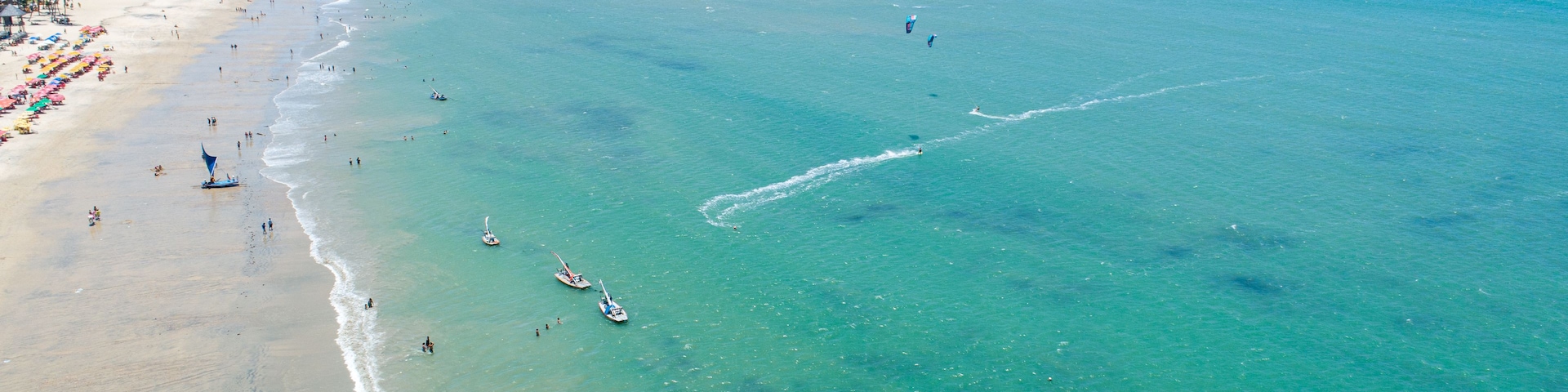 Uma praia com águas turquesa cristalinas, areal arenoso e vários barcos.