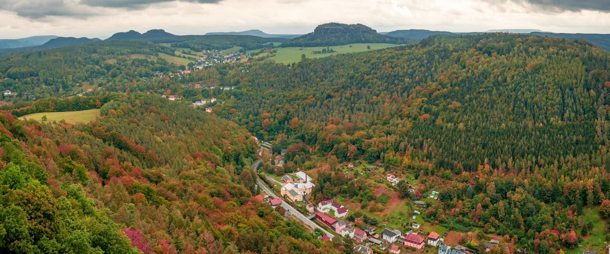 A mountainous landscape with a village nestled among trees with autumn foliage.