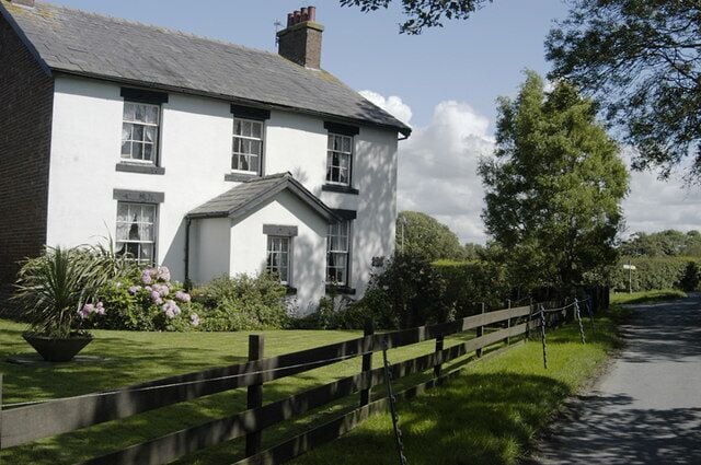 A white house with a grey roof, a wooden fence, and a road.