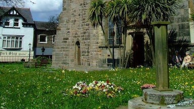 Une tour de pierre surmontée d’une horloge, entourée d’un jardin agrémenté de fleurs et de palmiers.