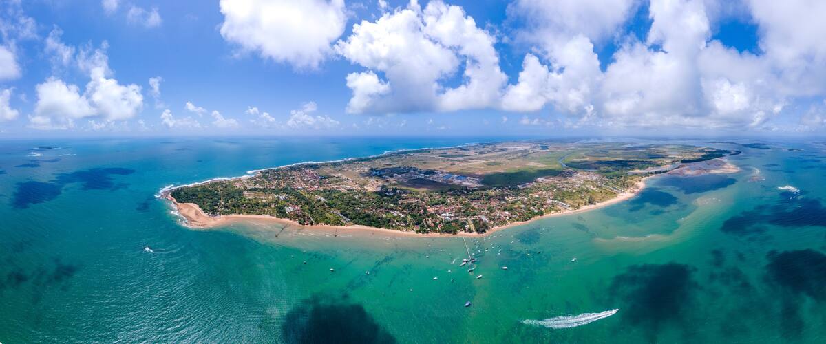An aerial view of a coastal island with a beach, clear waters, and scattered boats.