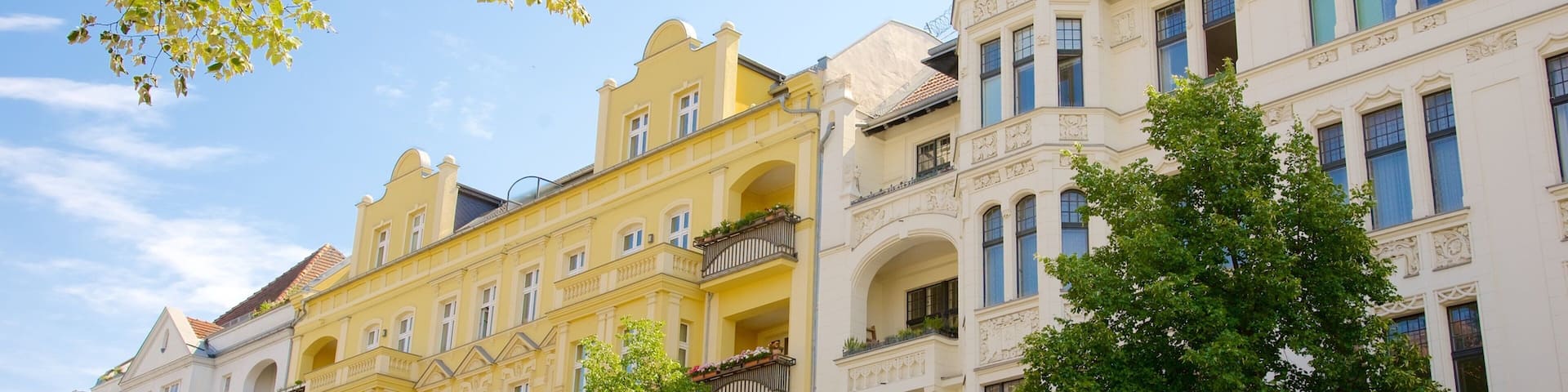 A row of historic yellow and white buildings with ornate balconies and a clear blue sky.