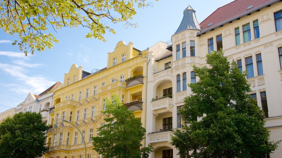 Une rangée de bâtiments historiques aux façades jaune et blanche, dotés de balcons richement décorés, se dressent sous un ciel d’un bleu limpide.